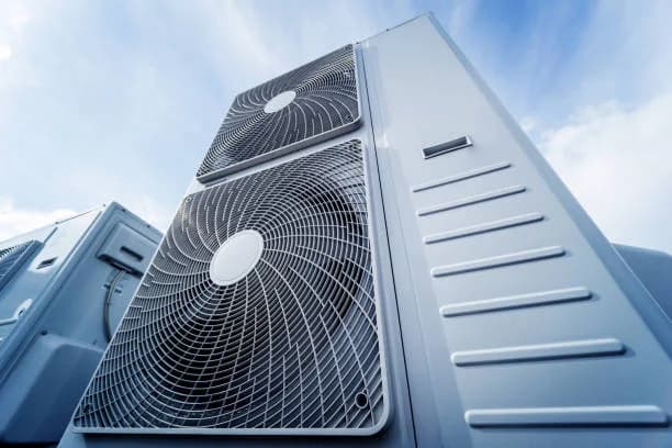 Close view of a large outdoor condenser fan and cabinet against a blue sky