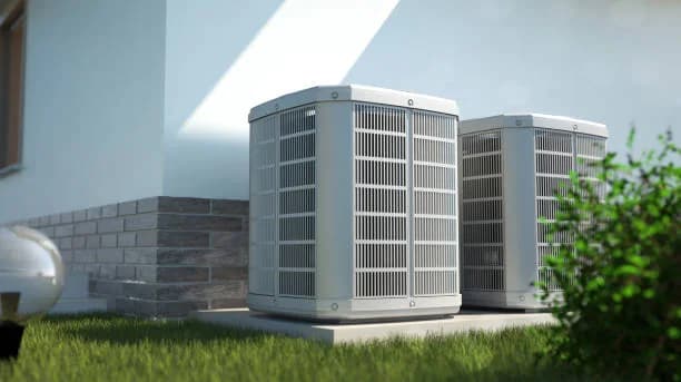 Two heat pump outdoor units beside a modern home on a lawn