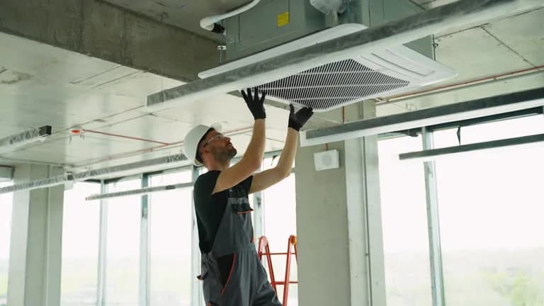Technician reaching up to a ceiling-mounted air handler vent panel