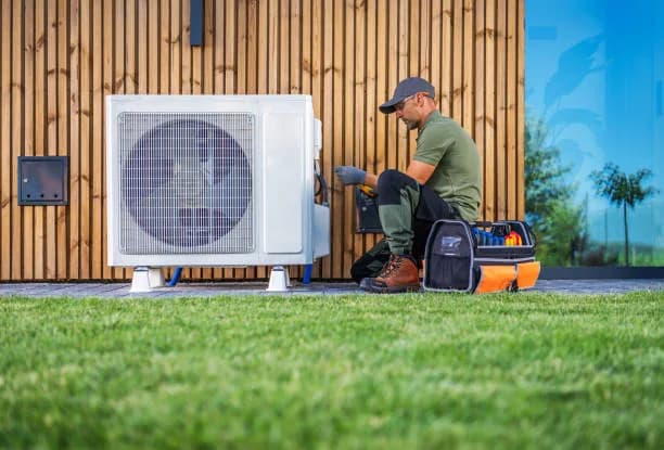Technician working beside a ductless mini-split outdoor unit on a wood-clad wall