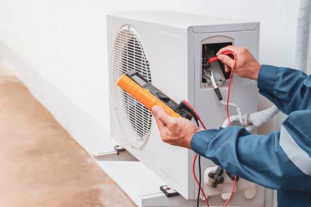 Technician testing electrical connections on an outdoor unit with a multimeter